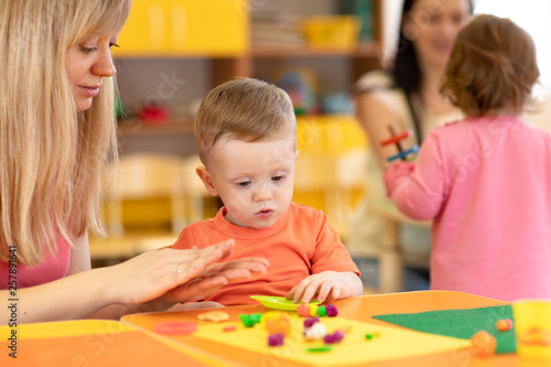 Kindergarten kid with teacher mould from plasticine on tablein nursery