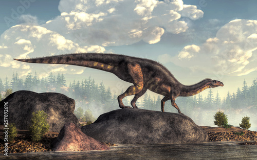 A plateosaurus stands on a large rock on the shore of an ancient lake.  This bipedal dinosaur leans forward to rest its hands on the ground as it looks out across the water. 3D Rendering    photo