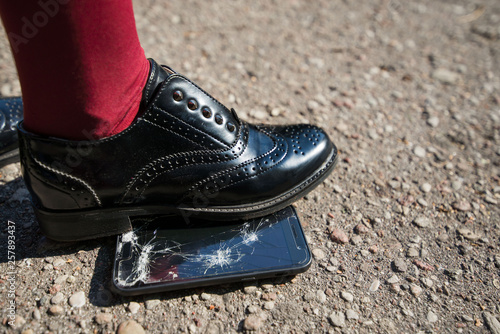 Woman step on the phone. Broken and damaged smartphone with cracks on glass screen laying on ground. Accident. Cell phone under shoe. Concept of warranty and lost smartphone 
