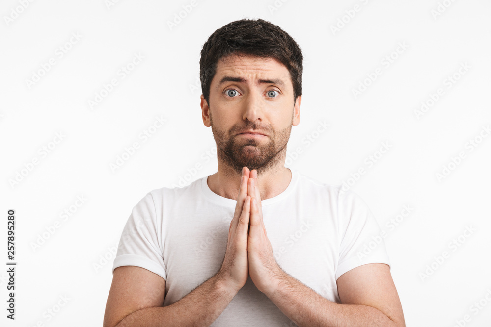 Image of unhappy man 30s with bristle in casual t-shirt holding palms together and praying Image of unhappy man 30s with bristle in casual t-shirt holding palms together and praying