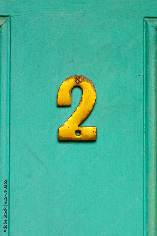 House number two with the 2 in golden bronze on a turquoise house door House number two with the 2 in golden bronze on a turquoise house door
