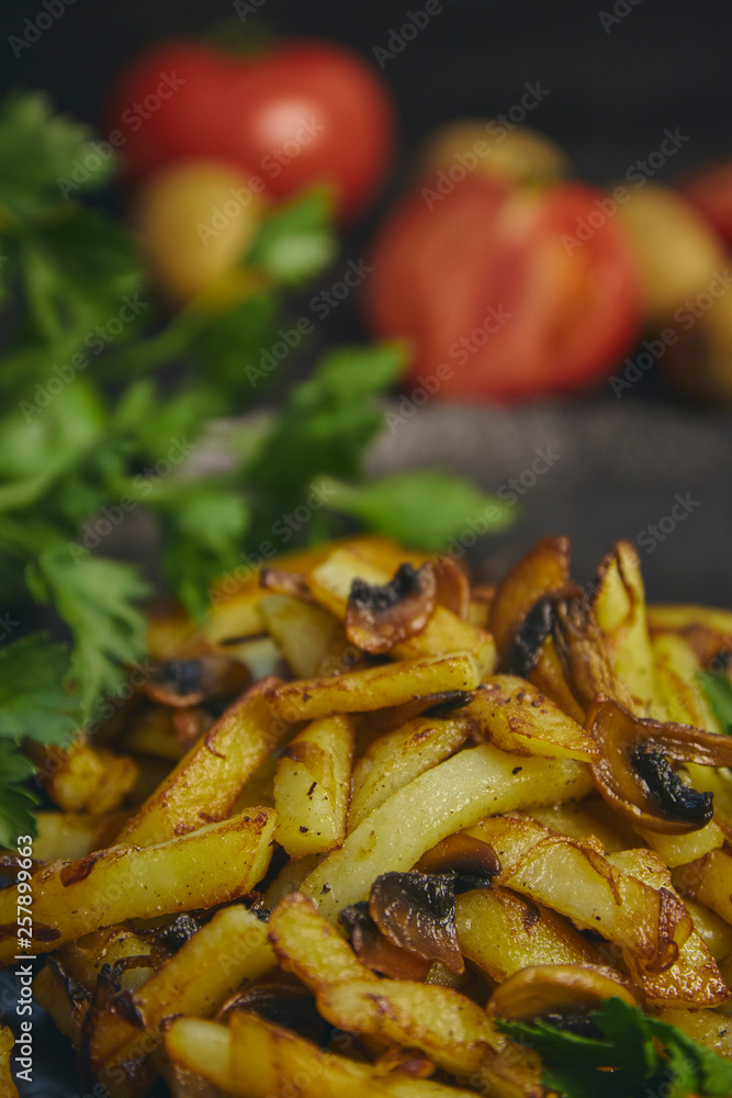Freshly cooked fried potatoes with onions and mushrooms close-up on a plate. ebony table. vertical view of the dish. Freshly cooked fried potatoes with onions and mushrooms close-up on a plate. ebony table. vertical view of the dish.