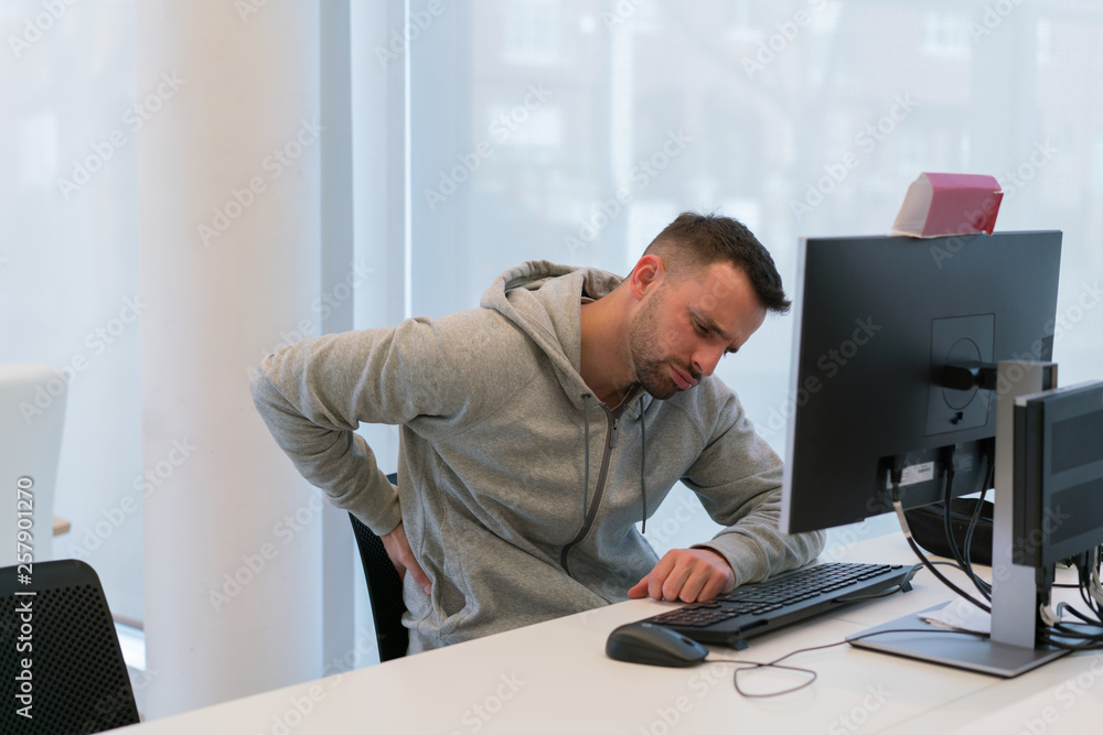 Young man with his hand on his back suffering pains from sitting for
