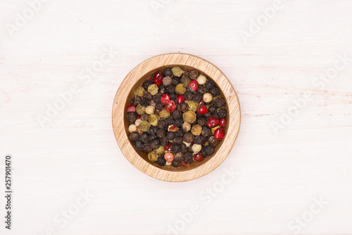 Lot of whole peppercorns of four colors with wooden bowl flatlay on white wood