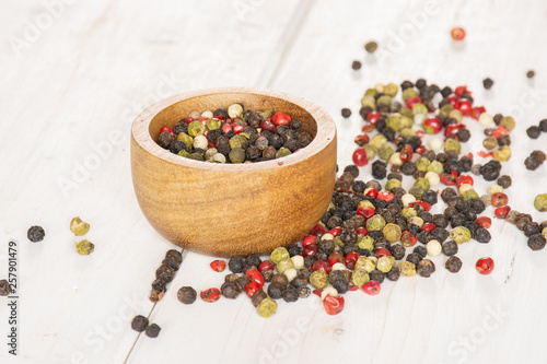 Lot of whole peppercorns of four colors with wooden bowl on white wood photo