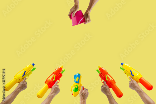 Hands holding plastic water gun and bucket ready to fight for Water or Songkran festival which celebrate in Thailand summer time on April with yellow color background.