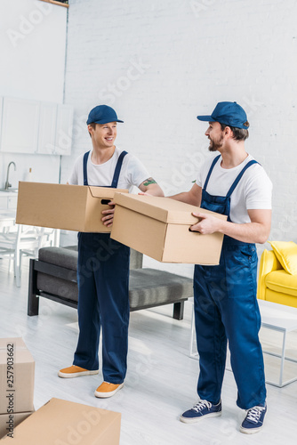 two smiling movers transporting cardboard boxes in apartment