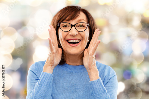 announcement and old people concept - smiling senior woman in glasses calling over festive lights background