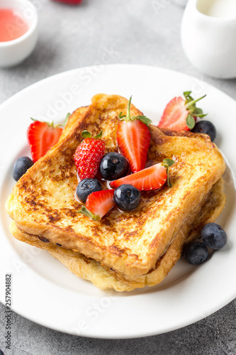 French toast with berries (blueberries, strawberries) and sauce, traditional sweet dessert of bread with egg and milk. Morning baking food