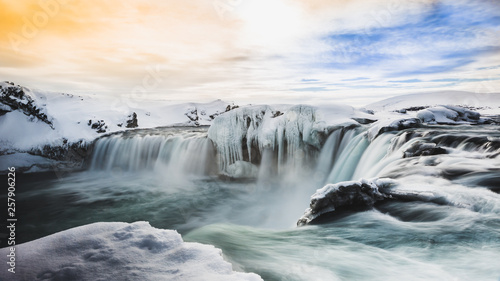 "godafoss" waterfall with yellow and blue sky.