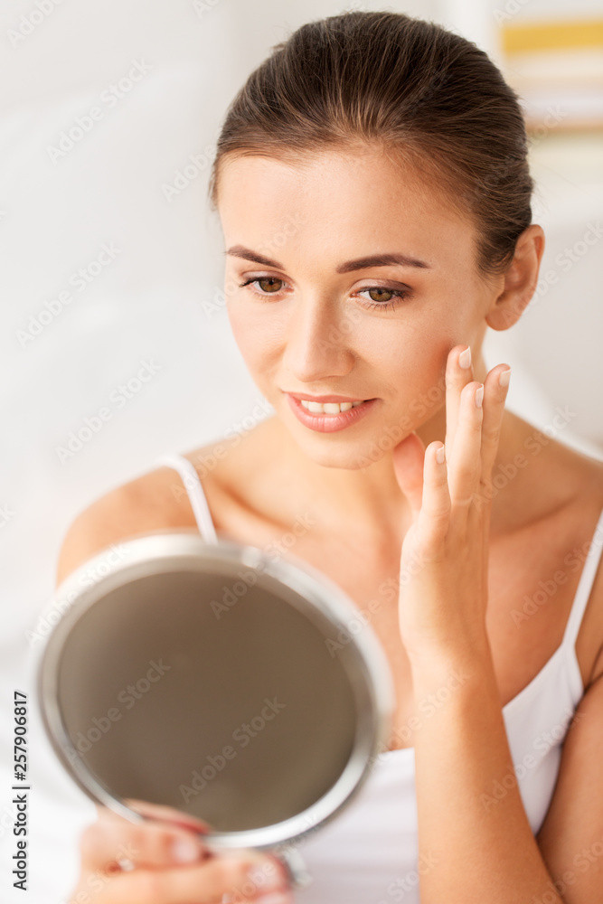beauty, skincare and people concept - beautiful woman looking to mirror and touching her face beauty, skincare and people concept - beautiful woman looking to mirror and touching her face