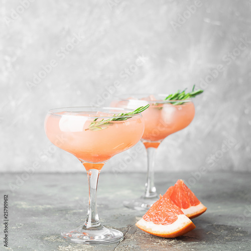 Drink grapefruit rosemary and ice in elegant glass goblets gray concrete background. Square frame Selective focus.