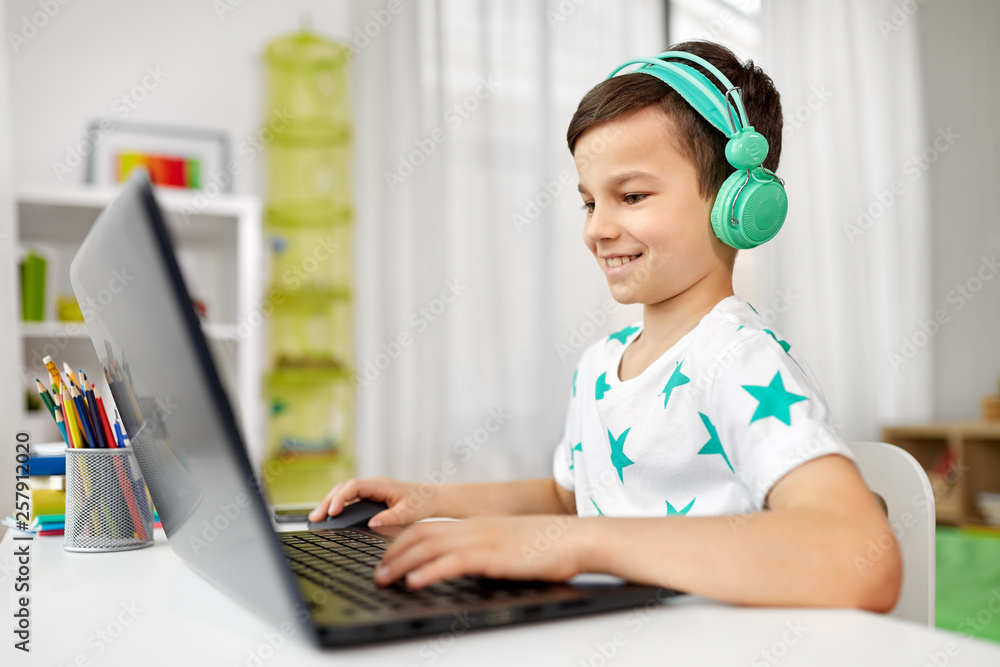 technology, gaming and people concept - boy in headphones playing video game on laptop computer at home technology, gaming and people concept - boy in headphones playing video game on laptop computer at home