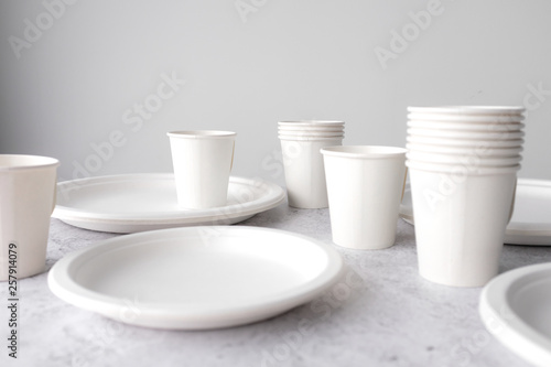 set of empty reusable disposable eco-friendly plates, cups, utensils on light white and grey concrete table top on white wall blurred background with copy space. Top view. 