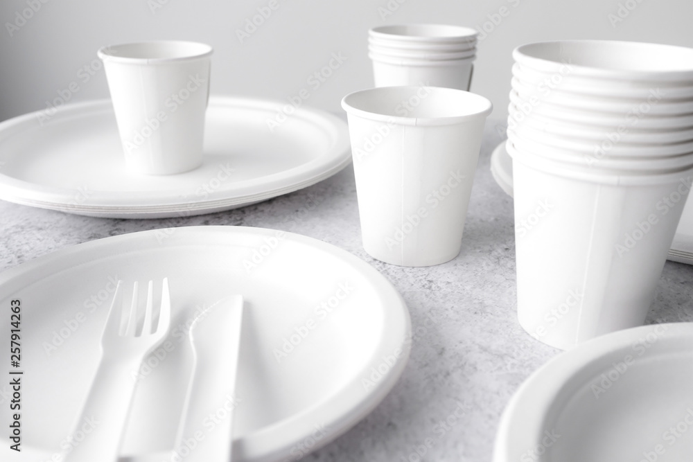 set of empty reusable disposable eco-friendly plates, cups, utensils on light white and grey concrete table top on white wall blurred background with copy space. Top view. set of empty reusable disposable eco-friendly plates, cups, utensils on light white and grey concrete table top on white wall blurred background with copy space. Top view.
