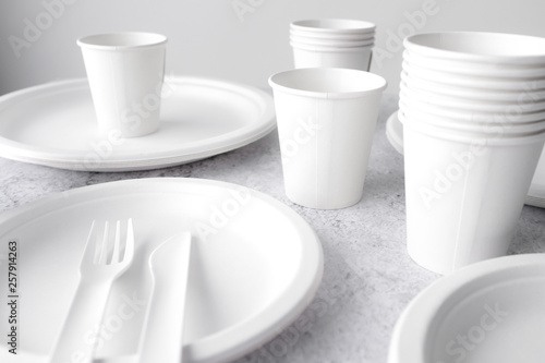 set of empty reusable disposable eco-friendly plates, cups, utensils on light white and grey concrete table top on white wall blurred background with copy space. Top view. 