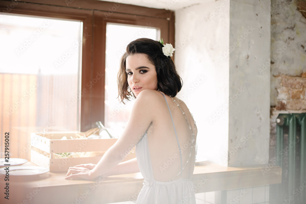 Obraz premium Model posing in a white long wedding dress indoors by the window. Advertising of wedding dresses