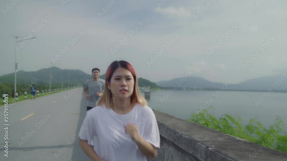 Slow motion - Asian runner couple running and jogging on street, Healthy young sporty sweet couple exercise near lake. Lifestyle fit and active couple exercise on street concept. Slow motion - Asian runner couple running and jogging on street, Healthy young sporty sweet couple exercise near lake. Lifestyle fit and active couple exercise on street concept.