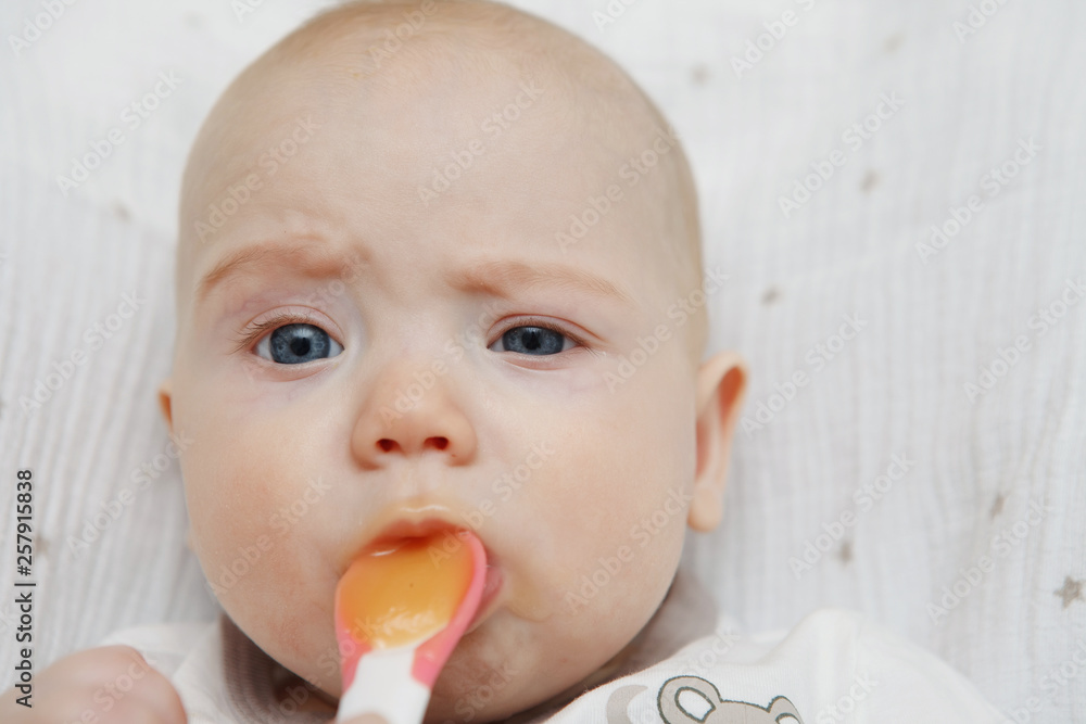 Beautiful Lovely five-month baby girl eating with a spoon. Healthy food. Maternal care. Childcare. Close-up. Beautiful Lovely five-month baby girl eating with a spoon. Healthy food. Maternal care. Childcare. Close-up.