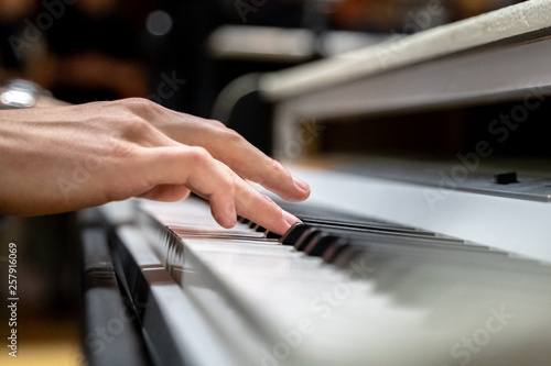Male hands with long fingers playing music on keyboard with white and black keys of a piano