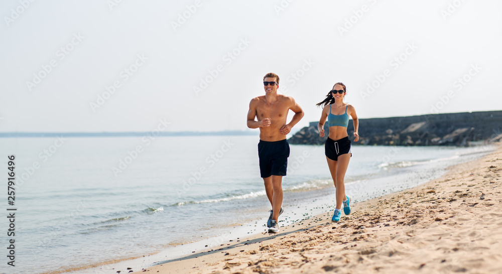 fitness, sport and lifestyle concept - happy couple in sports clothes and sunglasses running along summer beach fitness, sport and lifestyle concept - happy couple in sports clothes and sunglasses running along summer beach