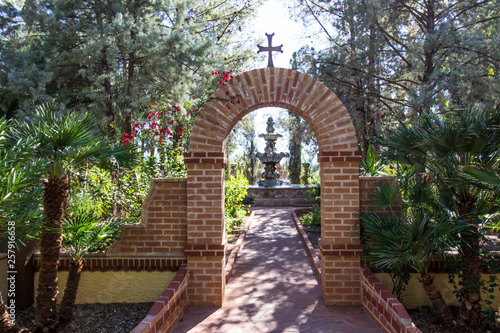 Arch With Cross Leading To Fountain In Monastery Garden