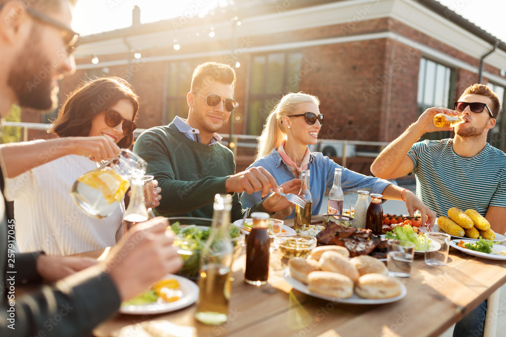 leisure and people concept - happy friends eating and drinking at barbecue party on rooftop
