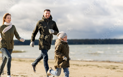 family, leisure and people concept - happy mother, father and little daughter running along autumn beach