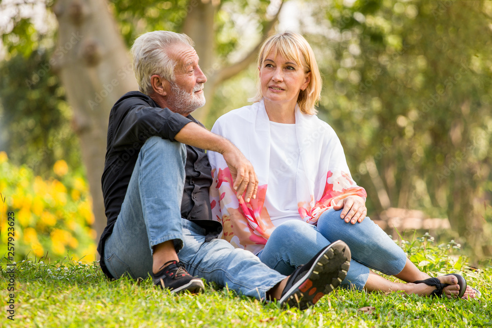 Fototapeta premium Happy senior couple relaxing at park together in morning time. old people sitting on grass in the autumn park . Elderly resting .mature relationships. family