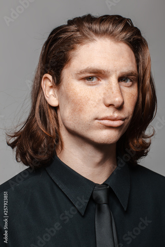 Portrait of a man with long hair and freckles, dressed in a black shirt and black tie