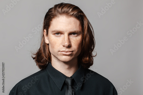 Portrait of a man with long hair and freckles, dressed in a black shirt and black tie