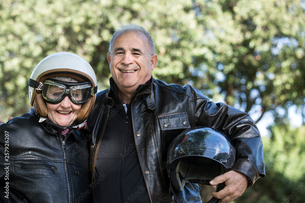 Coppia di motociclisti anziani sorride felice abbracciati al parco Coppia di motociclisti anziani sorride felice abbracciati al parco