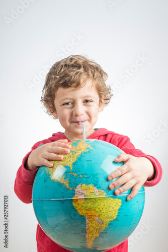 Child holding a globe in his arms and drinking from it with a straw.