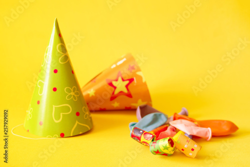 Birthday paper caps, balloons, colored party whistle on yellow background
