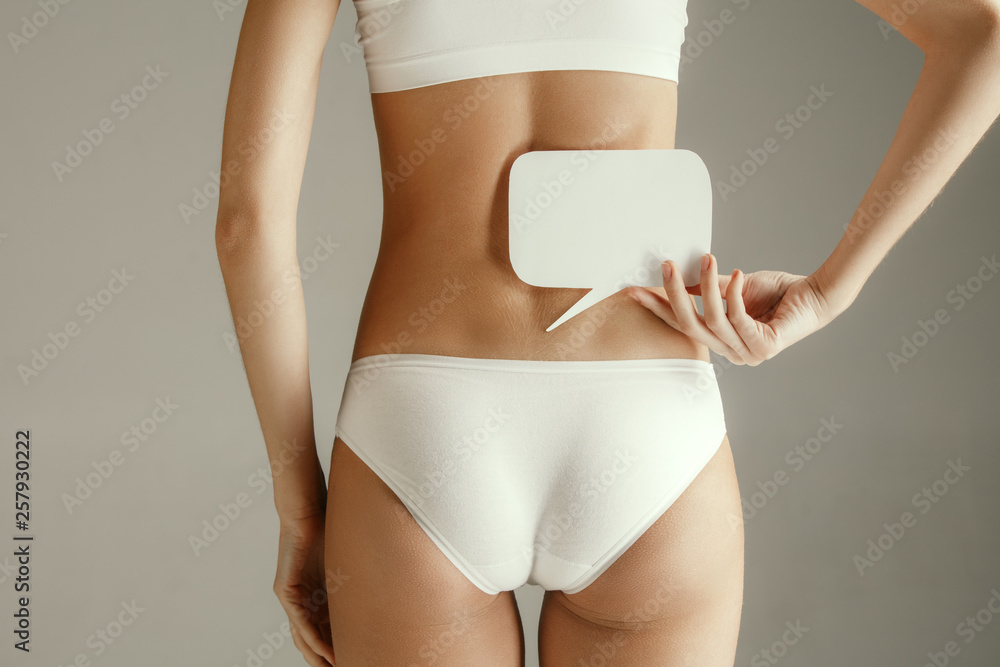 Woman health. Female model holding empty card near back. Young adult girl with paper for sign or symbol isolated on gray studio background. Cut out part of body. Medical problem and solution. - obrazy, fototapety, plakaty 