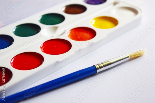 Watercolor paints and brushes for drawing on the table.
