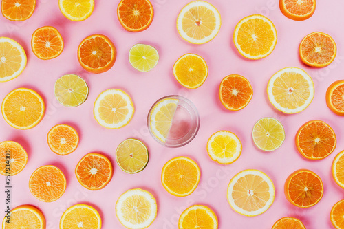 Flatlay of lemon water on pink background with various sliced citrus fruits on side