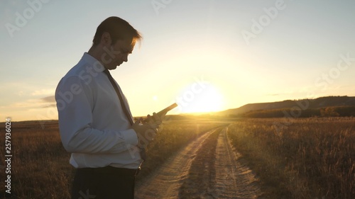 Businessman's fingers touch screen of tablet, smartphone. male hands are holding tablet and checking emails in park at sunset. male hand is typing a mobile message on the smartphone screen. © zoteva87