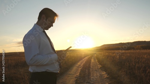 Businessman's fingers touch screen of tablet, smartphone. male hands are holding tablet and checking emails in park at sunset. male hand is typing a mobile message on the smartphone screen. © zoteva87