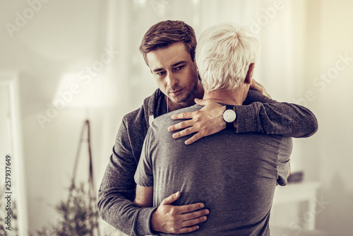 Canvas Print Twenty-years-old dark-haired kind male calmingly cuddling sick sorrowful aging g