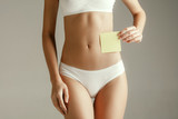 Woman health. Female model holding empty card near stomach. Young adult girl with paper for sign or symbol isolated on gray studio background. Cut out part of body. Medical problem and solution.