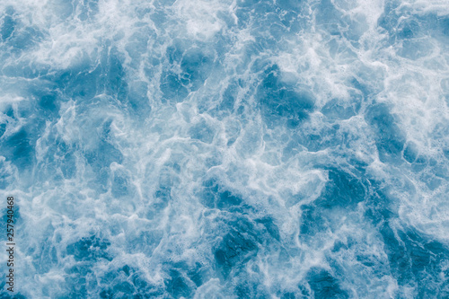 Pale blue sea surface with waves, splash, white foam and bubbles at high tide and surf, abstract background