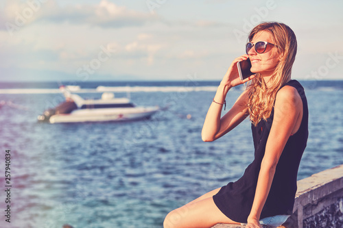 Attractive woman using cellphone while sitting near sea/ocean. © Kitja