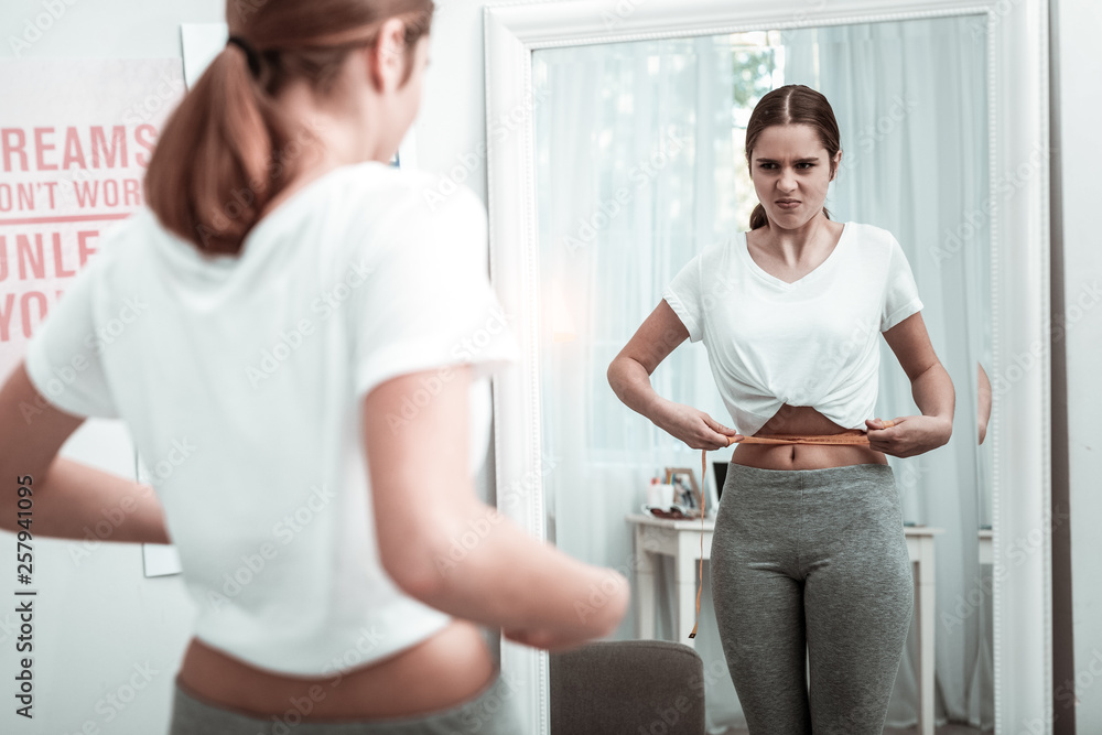 Teenager girl looking at her body parameters near the mirror Teenager girl looking at her body parameters near the mirror