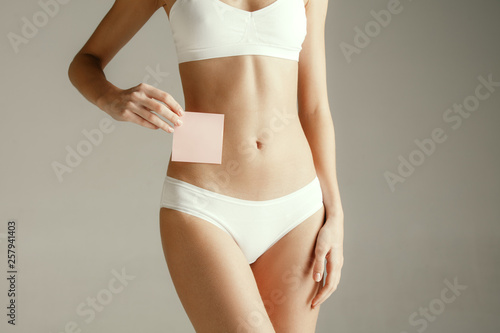 Woman health. Female model holding empty card near stomach. Young adult girl with paper for sign or symbol isolated on gray studio background. Cut out part of body. Medical problem and solution.