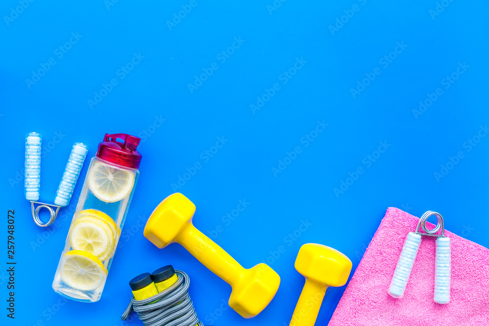 Fitness set with bars, towel, bottle of water and wrist builder on blue background top view mock up