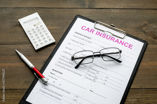 Car insurance form near glasses, calculator, pen on dark wooden background