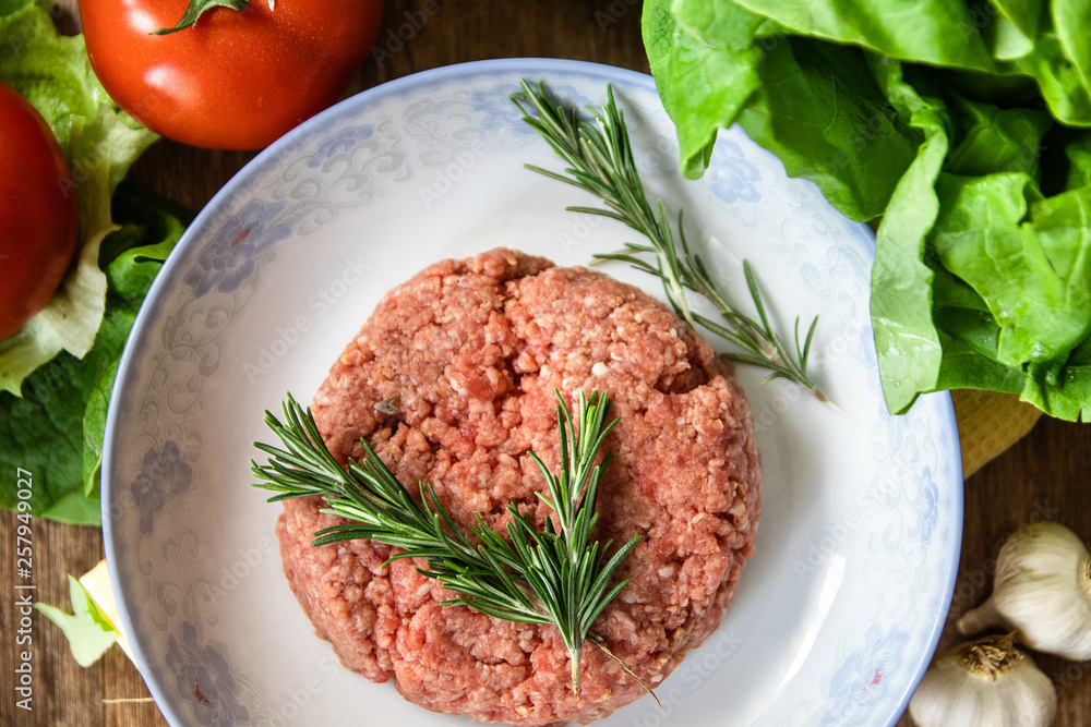 Fresh raw minced meat with rosemary on a plate and tomato, garlic, lettuce and onion on wooden table. Composition with meat and fresh organic vegetable. Fresh raw minced meat with rosemary on a plate and tomato, garlic, lettuce and onion on wooden table. Composition with meat and fresh organic vegetable.
