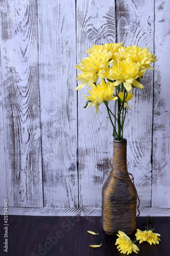 Bouquet of yellow chrysanthemum flowers in a vintage bottle against the white wooden background