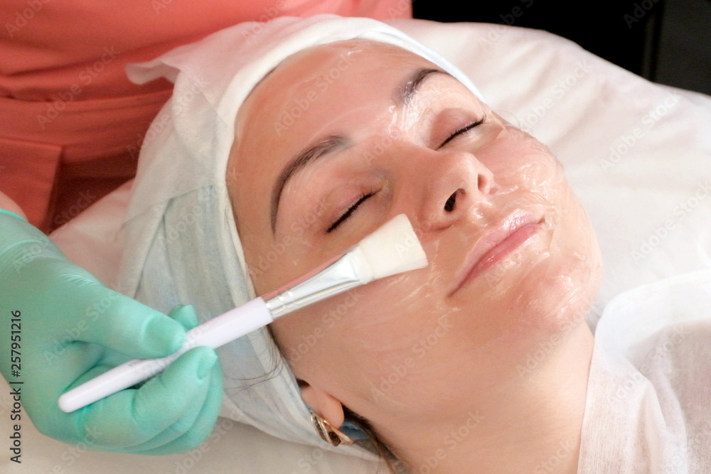 The procedure for applying a face mask in the beauty salon. Cosmetologist gloves smears brush gel on the girl's face. Cosmetology. Beauty The procedure for applying a face mask in the beauty salon. Cosmetologist gloves smears brush gel on the girl's face. Cosmetology. Beauty